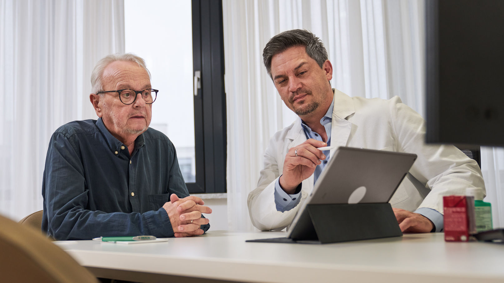 Oncólogo consultando a un paciente con cáncer y ofreciendo asesoramiento a través del iPad 