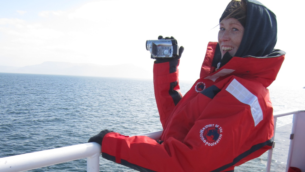 Mujer con abrigo de invierno grueso y capucha que sostiene una cámara en un barco